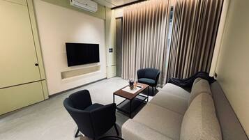 A modern living room with a flat-screen TV, a sofa, two armchairs, and a coffee table.