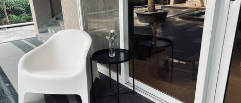 A modern bathroom with a white bathtub, a small black table with a vase, and a glass door leading to an outdoor area with a palm tree and tiled flooring.