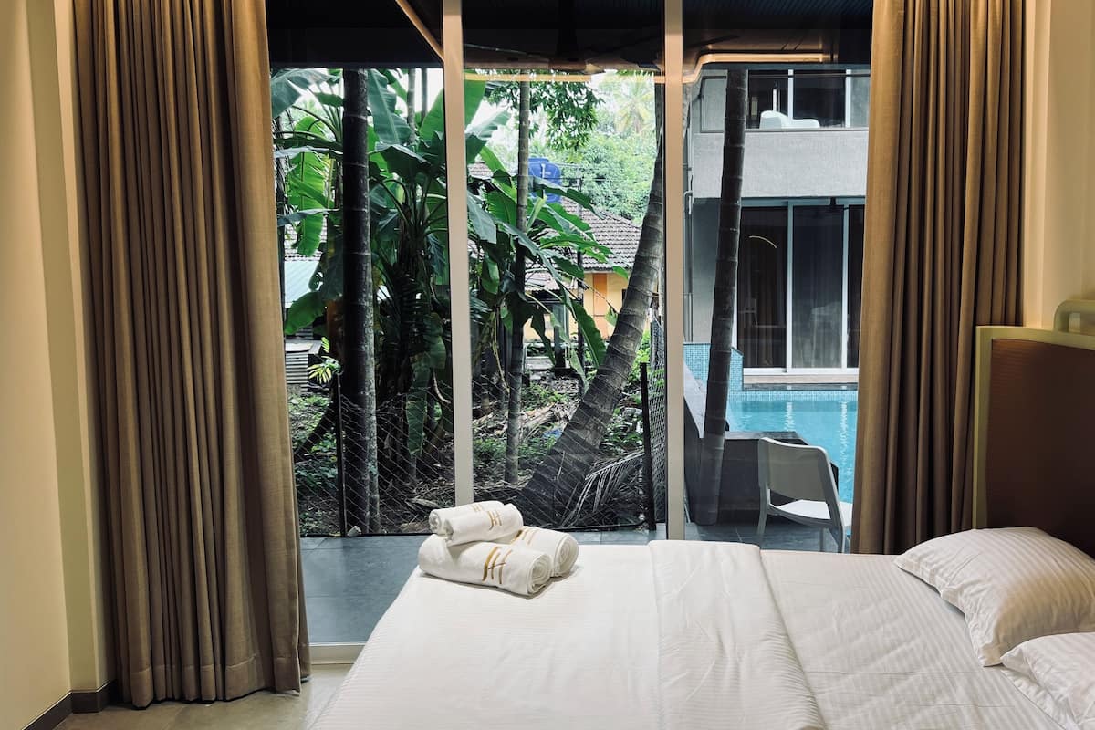 Une chambre d’hôtel avec un lit, une vue sur une piscine et un balcon agrémenté de plantes.