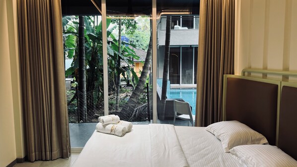 Habitación de hotel con cama, vista a una piscina y balcón con plantas.