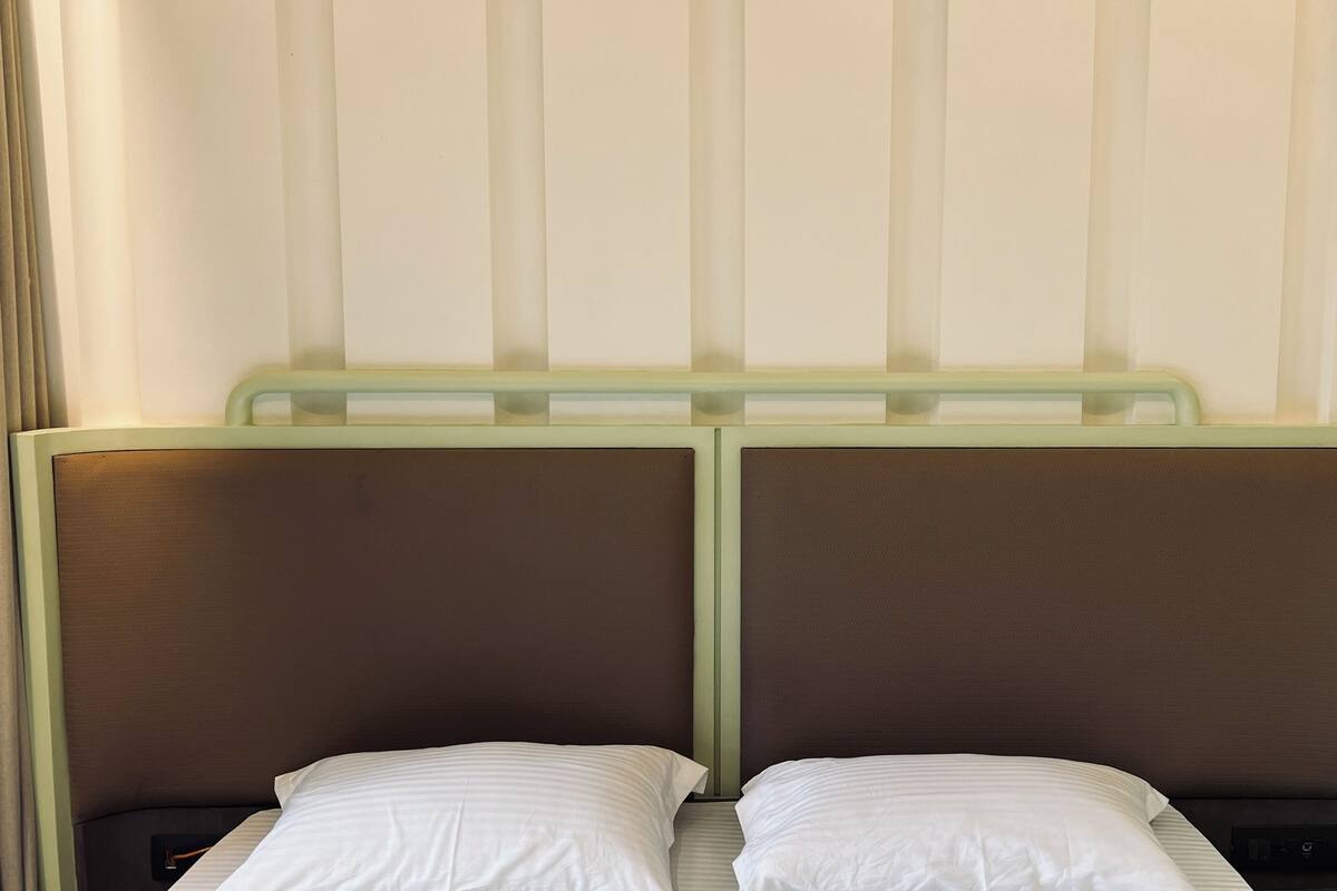 Un lit double avec deux oreillers, une tête de lit dotée d’un cadre vert clair et un mur sobre orné de lignes verticales.