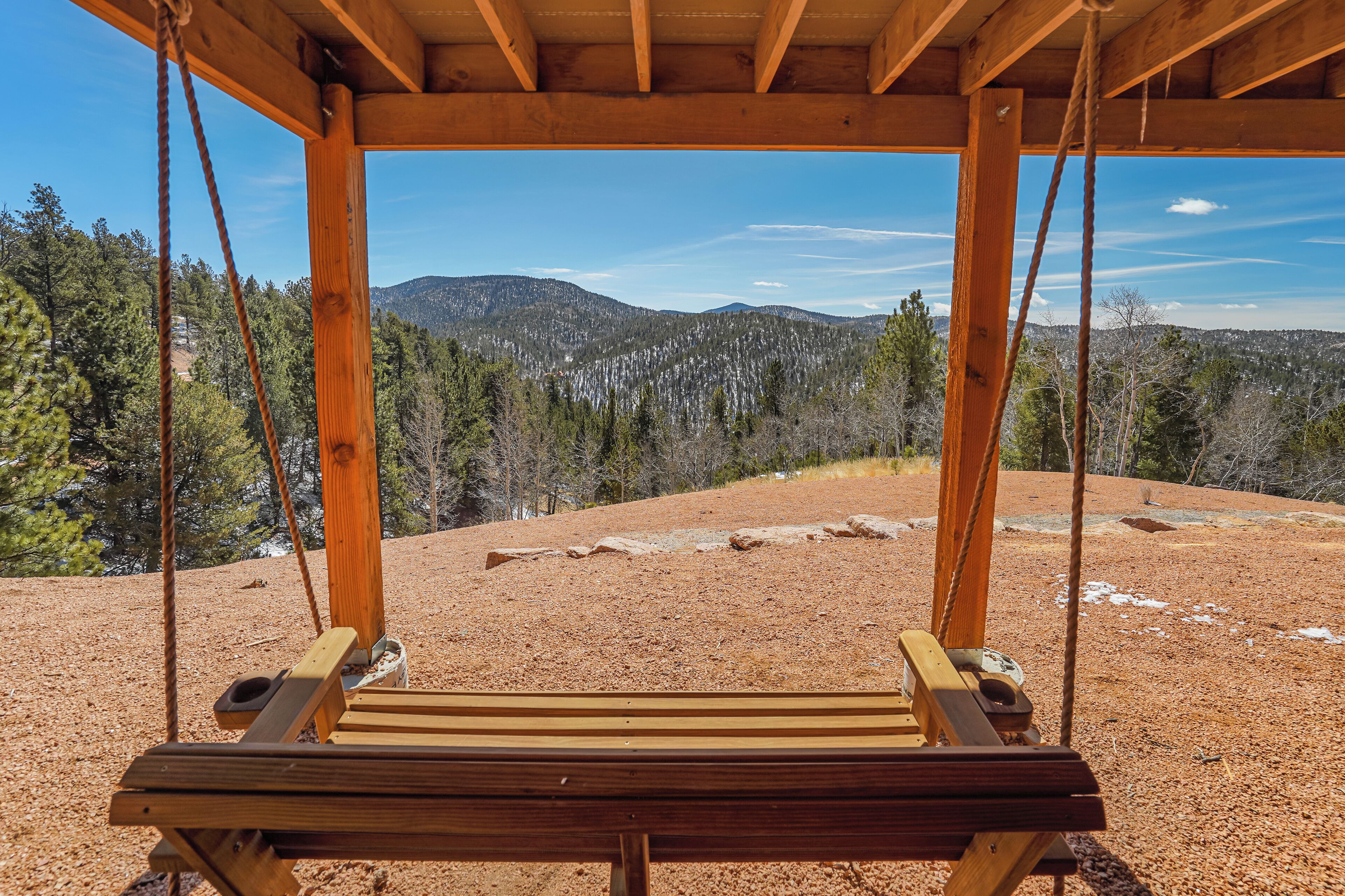A wooden swing chair with a view of a forested mountain range.