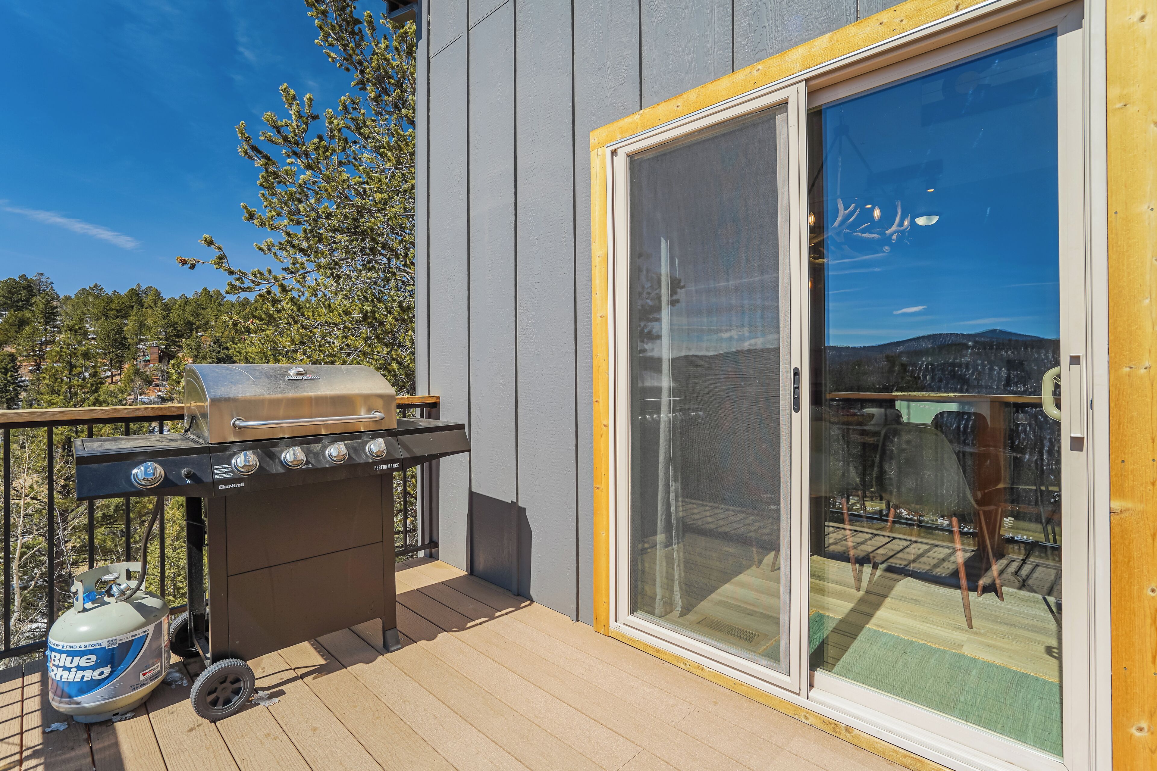 A deck with a barbecue grill and a propane tank, a sliding glass door, and a view of a mountainous landscape.