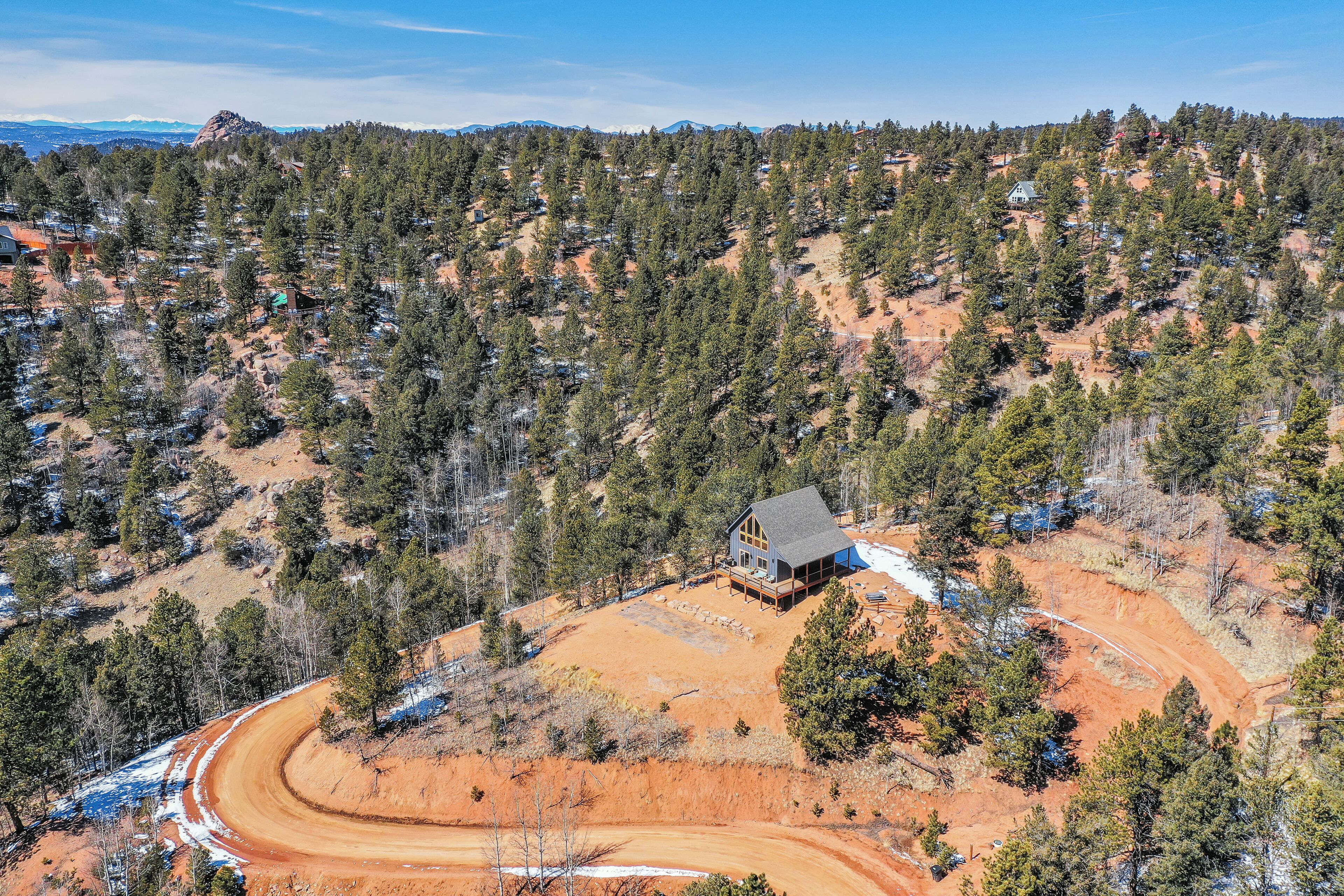 A remote cabin surrounded by a forested hillside with a dirt road leading to it.