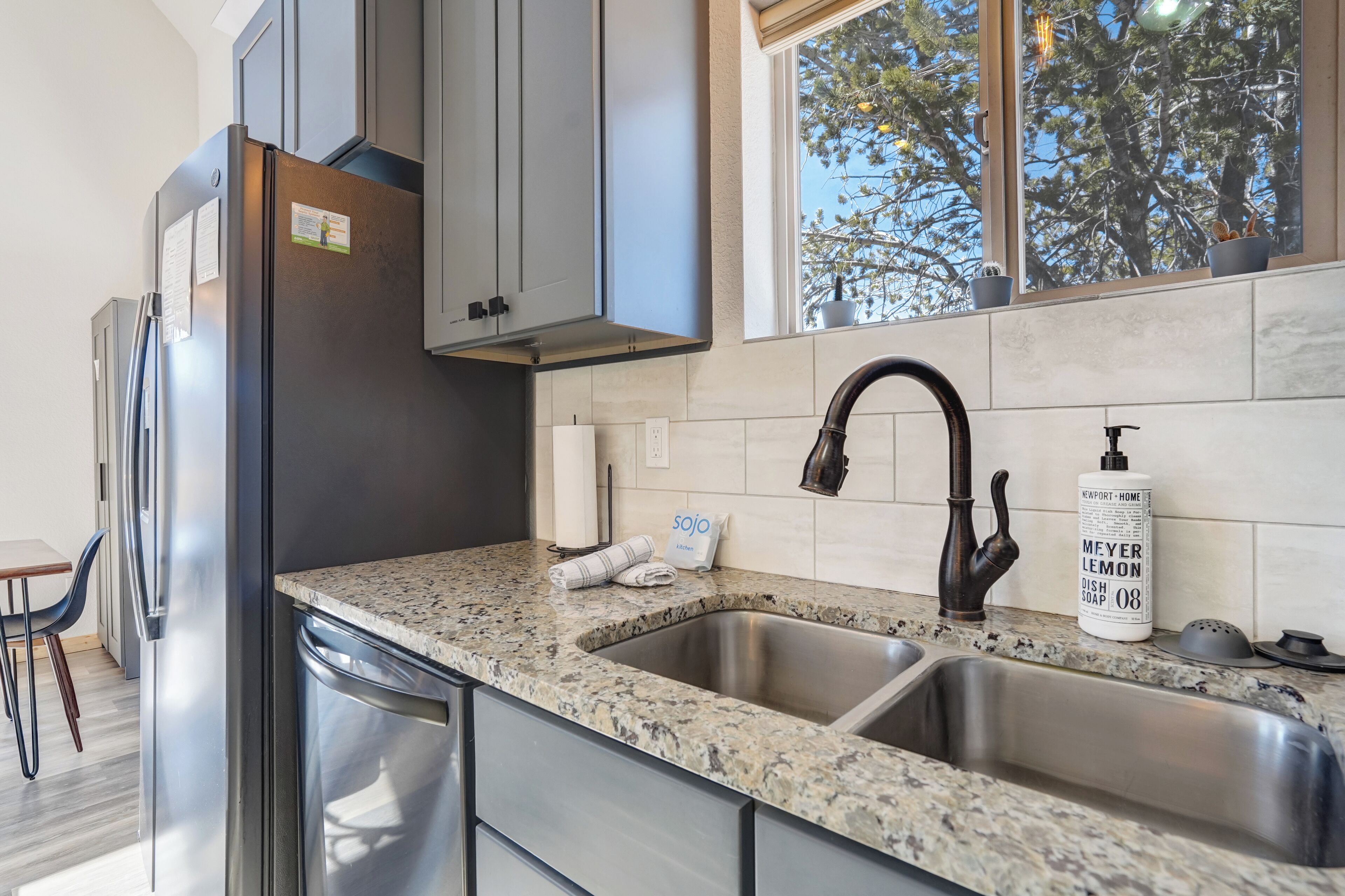 A modern kitchen with granite countertops, stainless steel appliances, and a window with a view of trees.