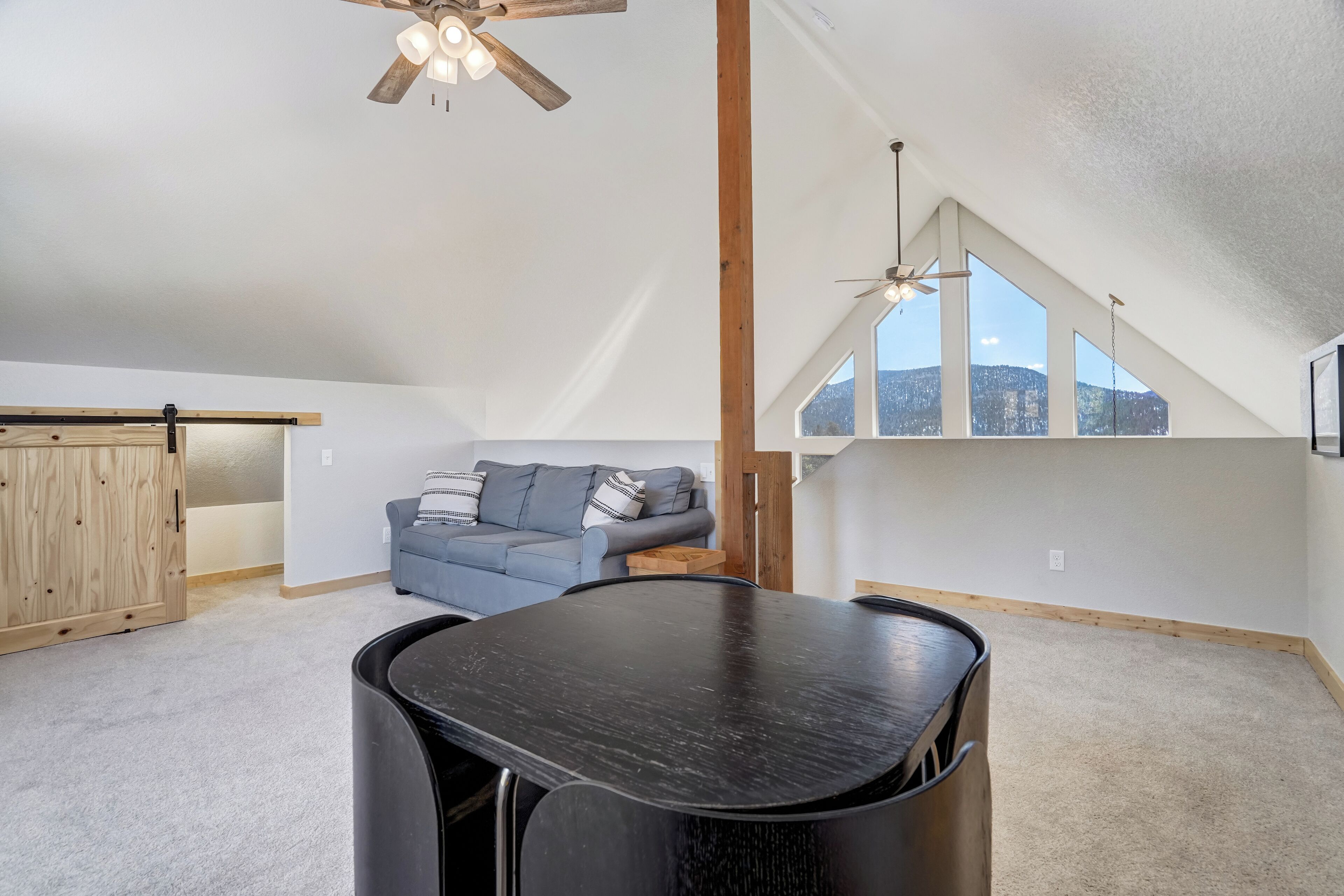 A spacious loft with a high ceiling, a dining table, a sofa, and large windows offering a view of the mountains.