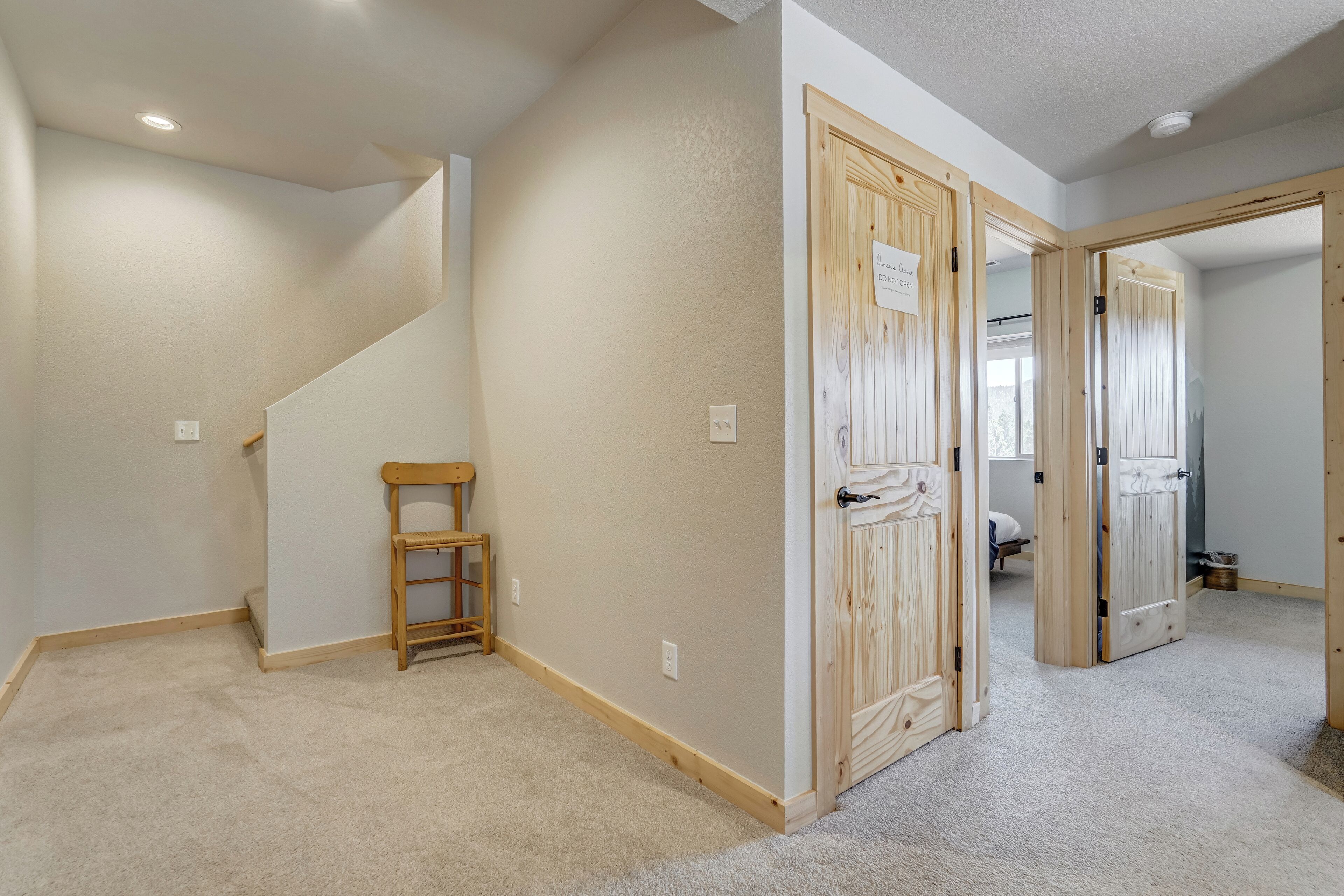 A room with a carpeted floor, a wooden chair, and a door with a sign.