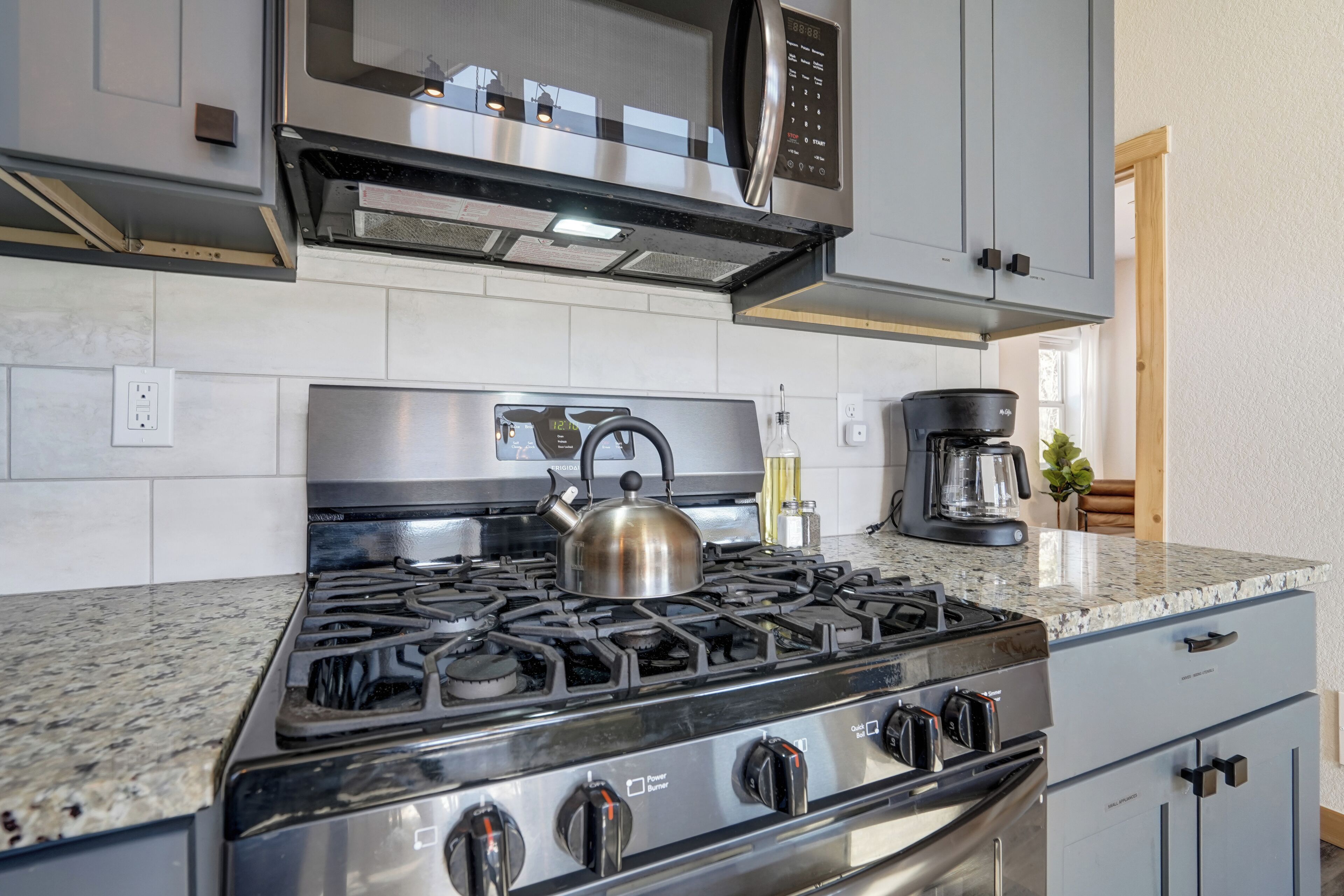 A kitchen with a stainless steel stove, a kettle, and a coffee maker.