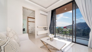 Una habitación de hotel moderna con balcón, un sofá blanco, una mesita con un florero y vistas a la montaña.