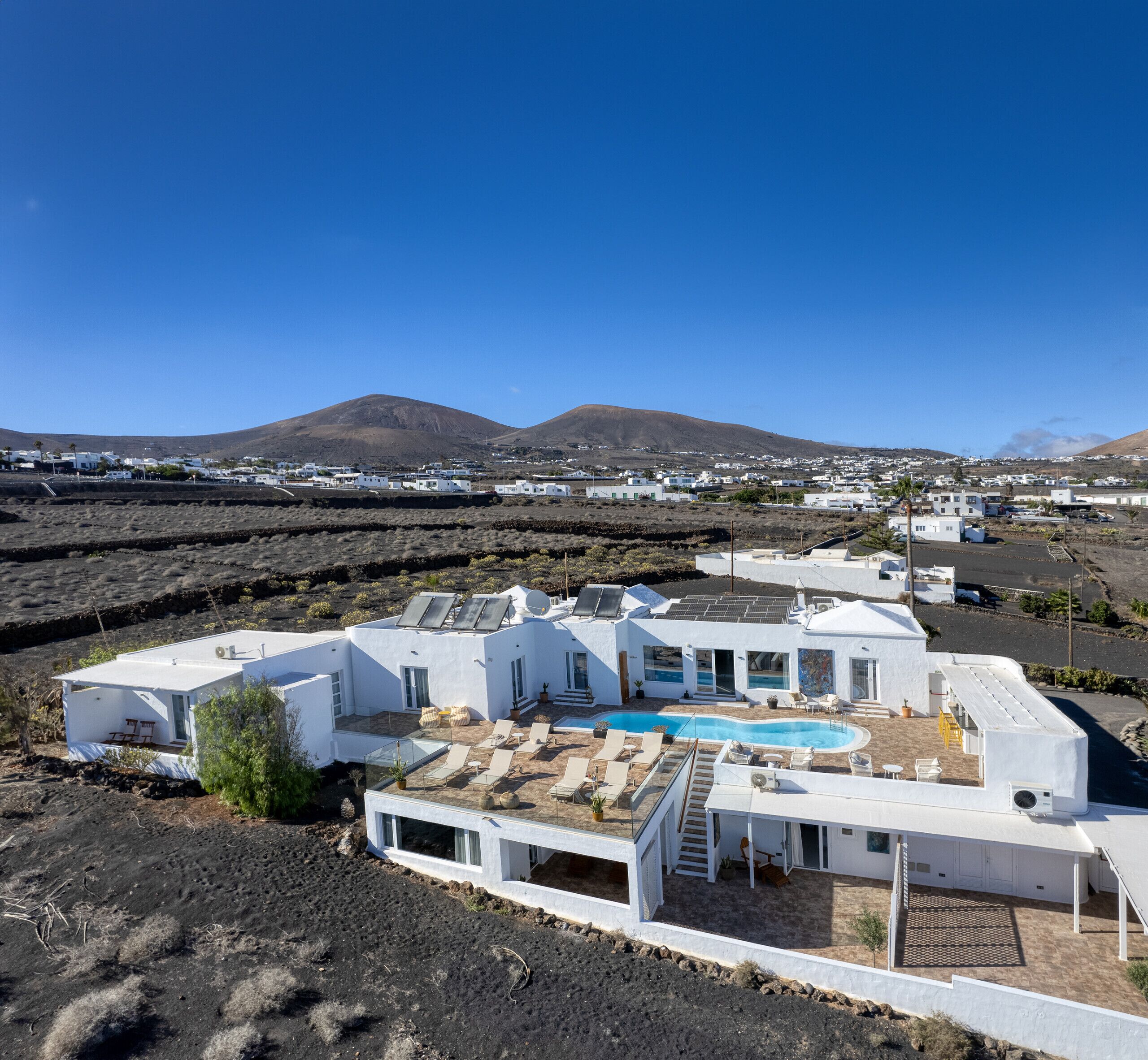 Una villa blanca y moderna con piscina, rodeada por un paisaje árido y montañas al fondo.