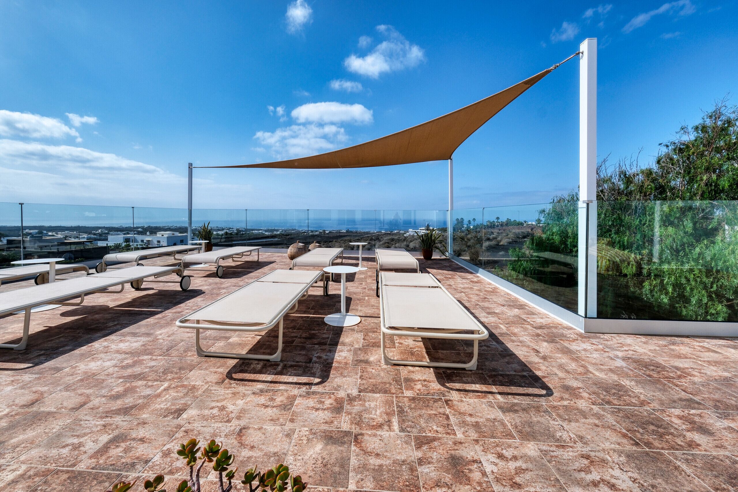 A rooftop terrace with sun loungers, a table, and a large shade sail.