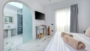 Ett modernt hotellrum med en stor säng, en tv som är monterad på väggen, ett badrum med marmorgolv och ett stort fönster med gardiner.
