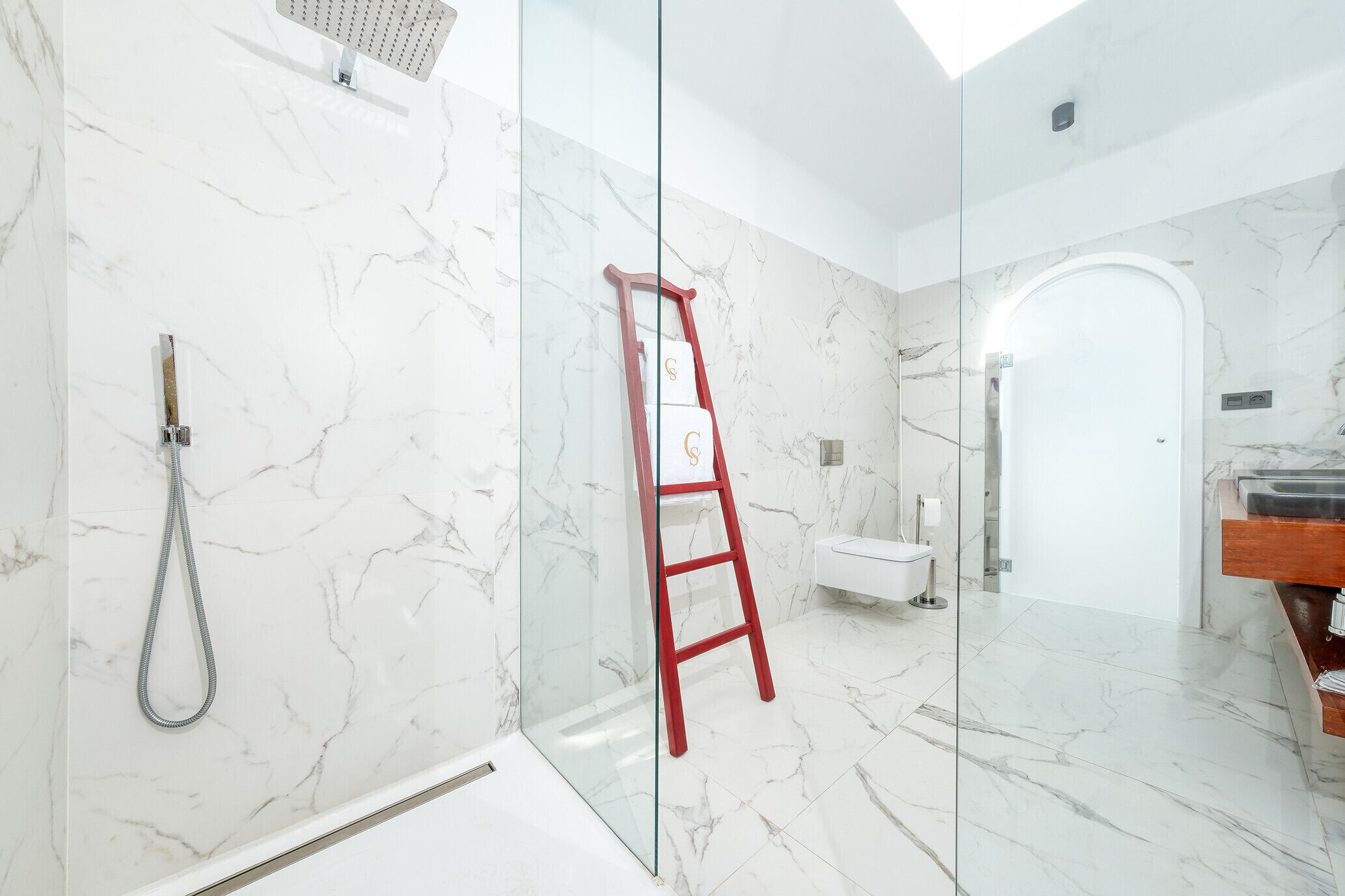 A modern bathroom with a glass shower enclosure, a marble-tiled floor, and a red ladder leaning against the wall.
