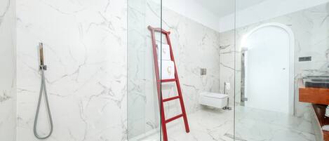A modern bathroom with a glass shower enclosure, a marble-tiled floor, and a red ladder leaning against the wall.
