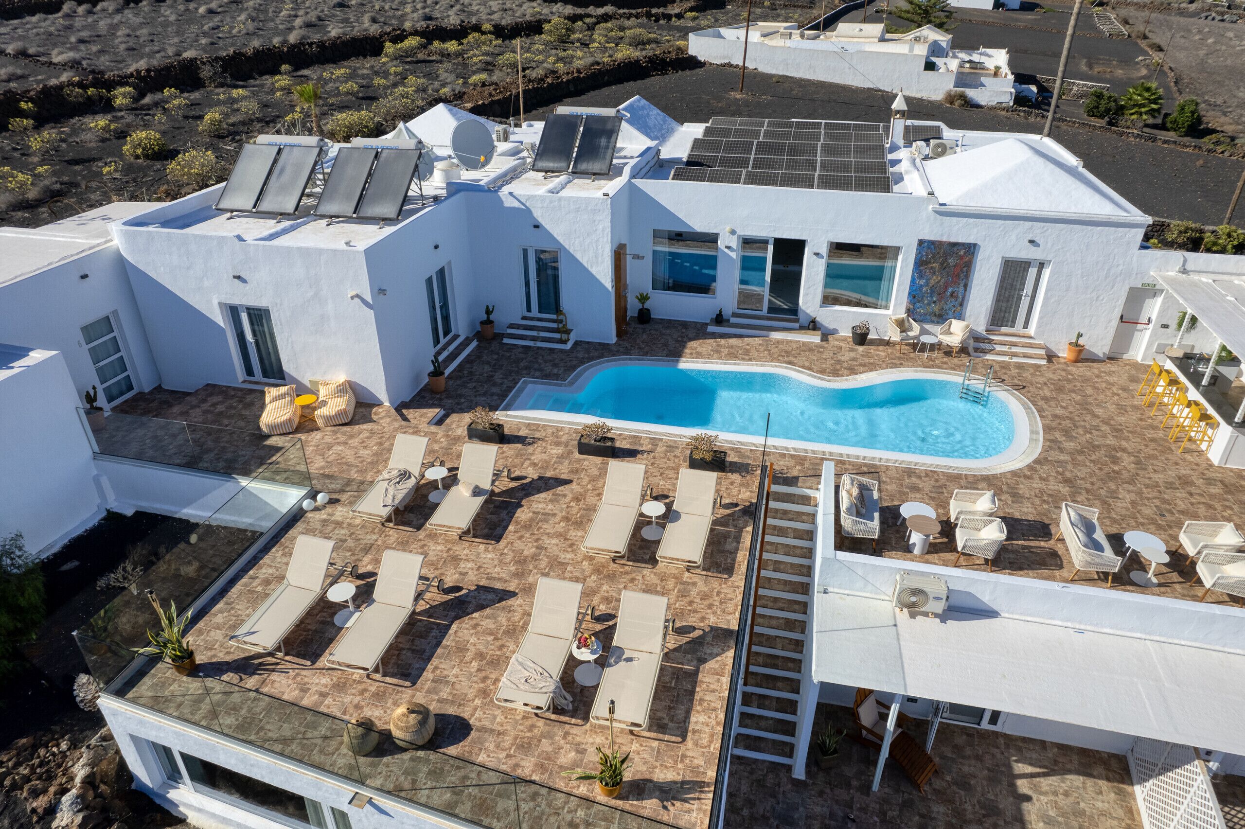 A modern white villa with a swimming pool, sun loungers, and solar panels.