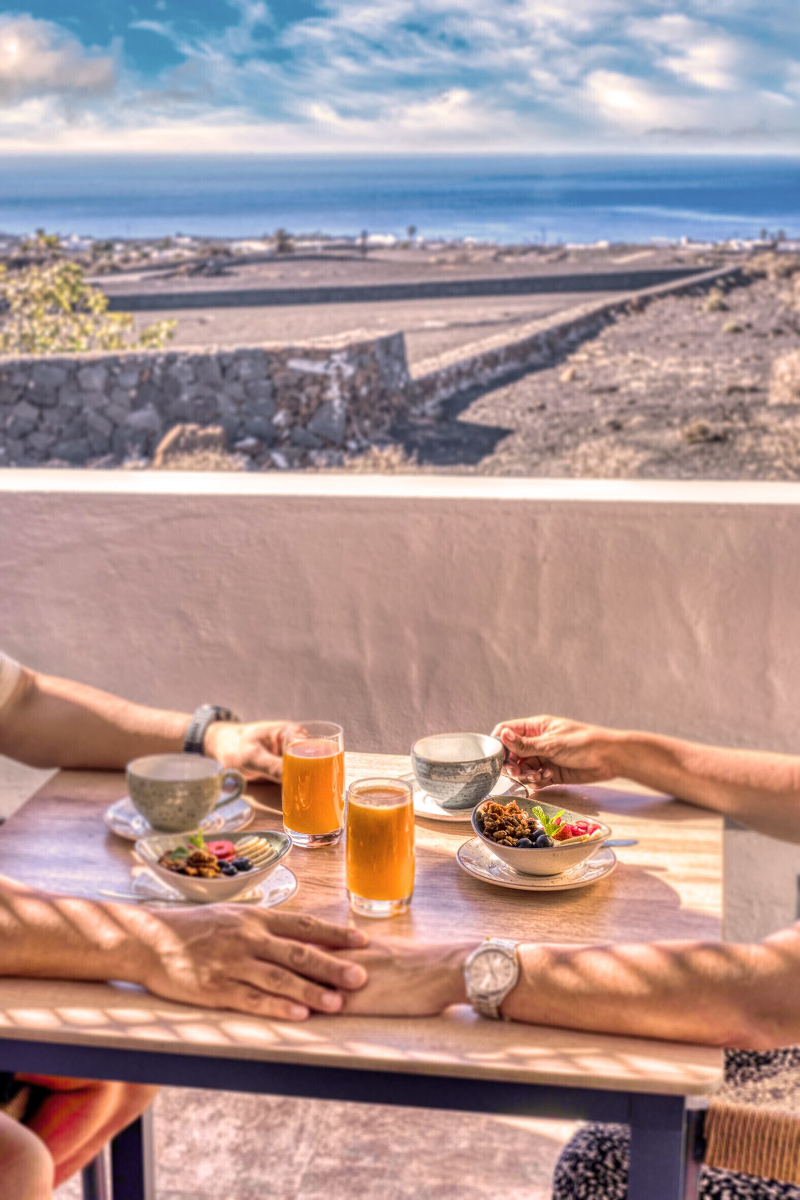A table with breakfast items and drinks, overlooking a coastal landscape.