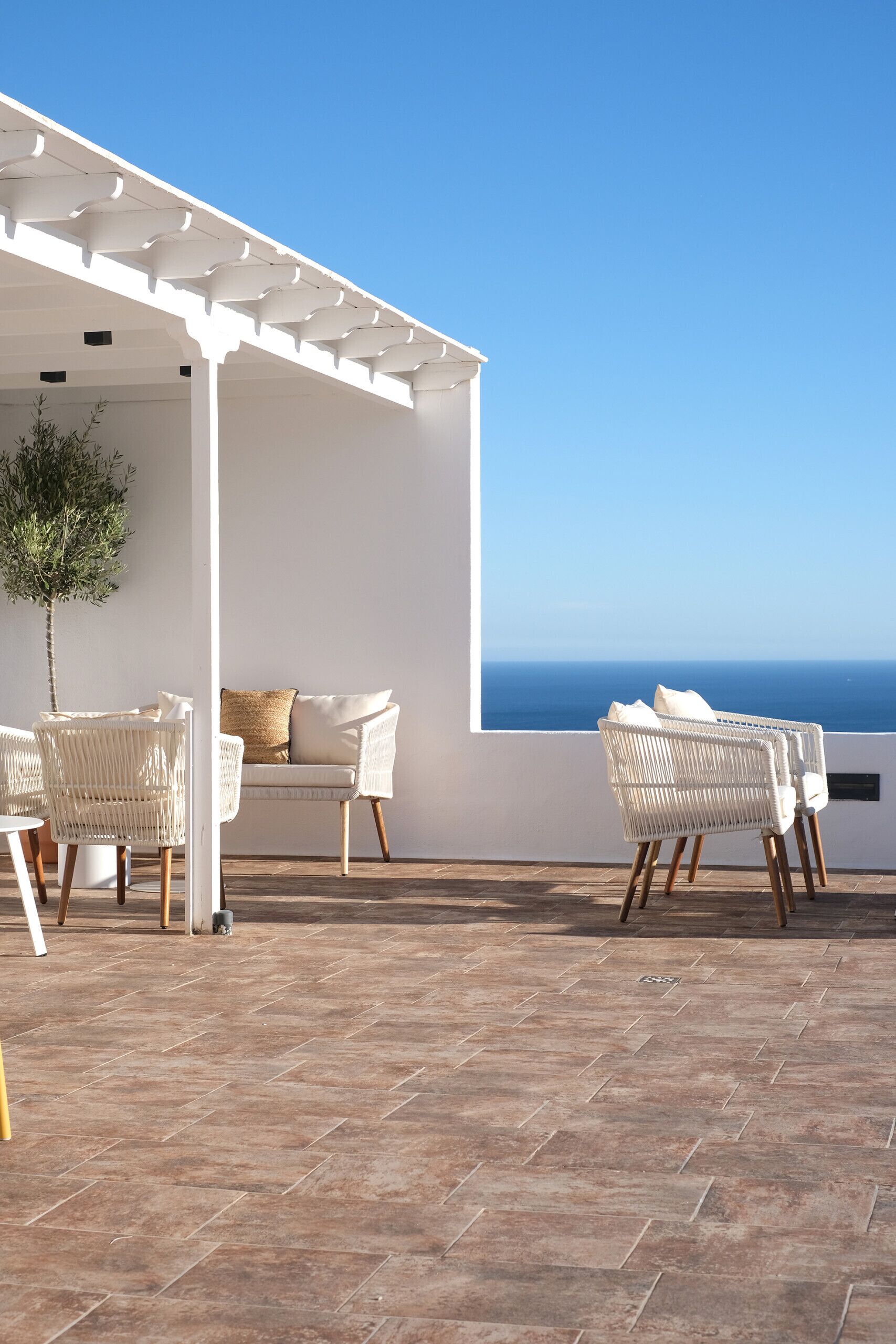 A terrace with white wicker furniture, a white sofa, and a potted plant.