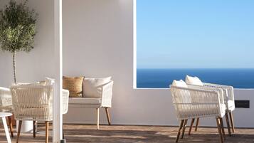 A terrace with white wicker furniture, a white sofa, and a potted plant.