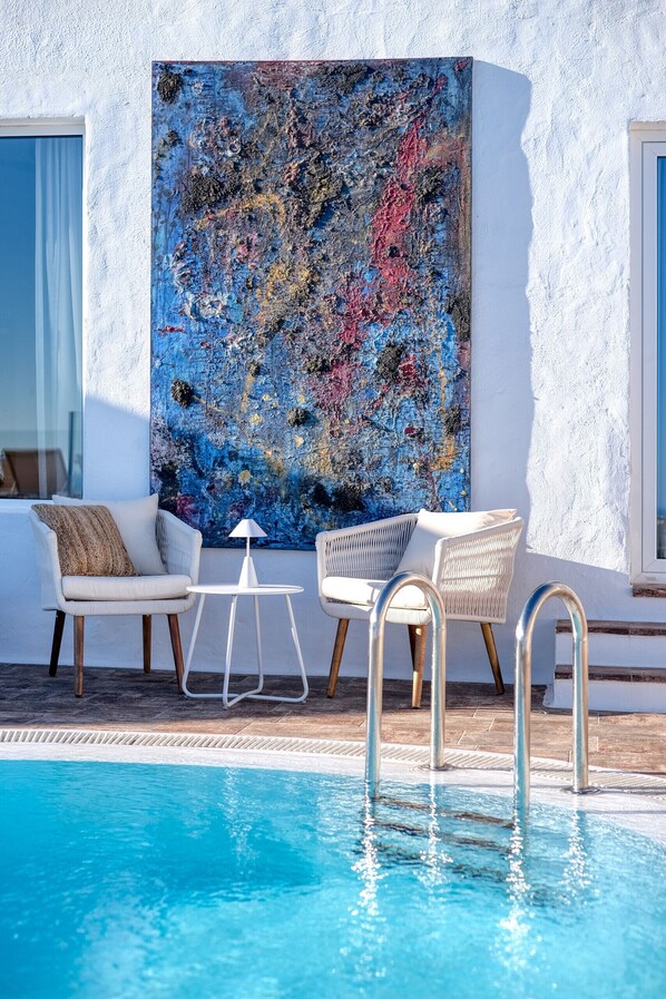 A poolside area with two white wicker chairs, a small white table, and a large abstract painting on the wall.