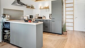 A modern kitchen with grey cabinets, a central island, wooden beams on the ceiling, and a built-in stove. - "Kanerva" - 100m to the fjord by Interhome (Storvorde)