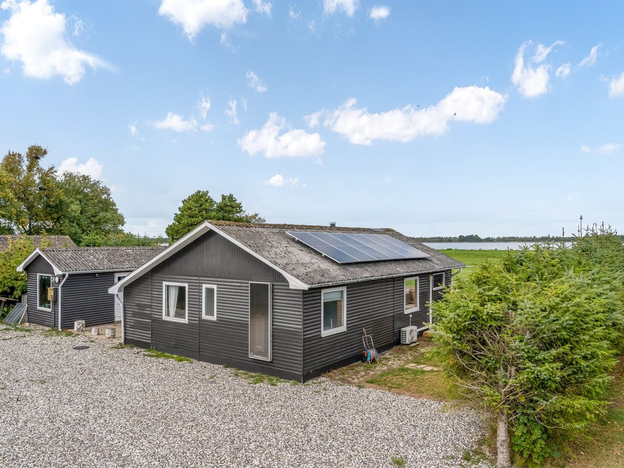 A two-story cabin with a gravel driveway and solar panels on the roof.