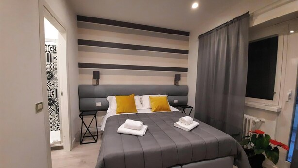 Un dormitorio moderno con una cama grande, ropa de cama gris, un cabecero gris y una ventana con cortinas.