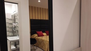 Una habitación de hotel moderna con baño, cama con ropa de cama estampada y una pequeña zona de escritorio.