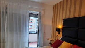 Habitación de hotel con cama, mesita de noche, lámpara y vista a un edificio a través de la ventana.