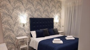 Habitación de hotel con una cama grande, mesitas de noche blancas, un escritorio blanco y una silla.