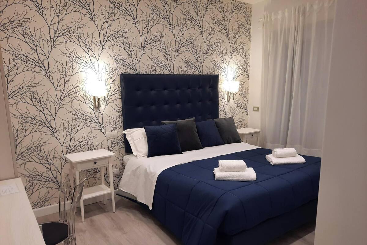 Ein Hotelzimmer mit einem großen Bett, Nachttischen in Weiß, einem weißen Schreibtisch und einem Sessel.