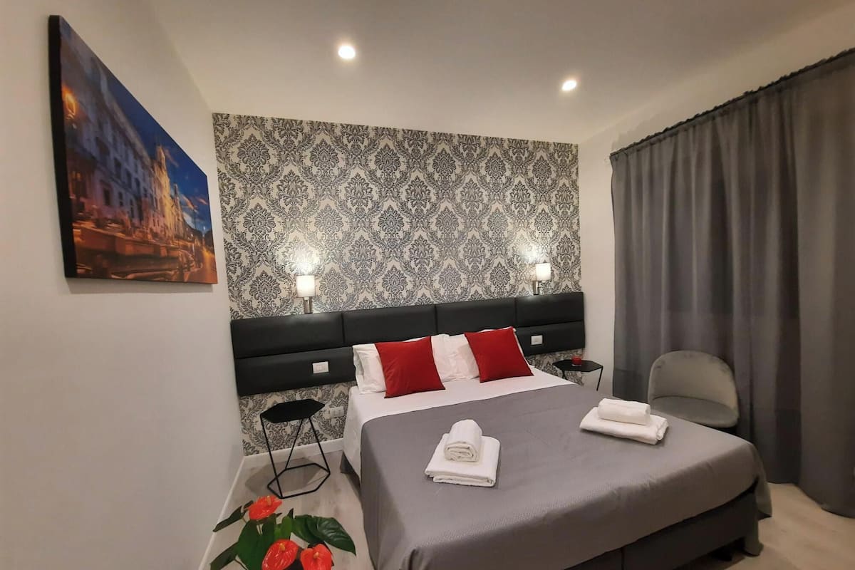 Ein Hotelzimmer mit einem großen Bett, einem Nachttisch, einem Sessel, einer Zimmerpflanze und einem Gemälde an der Wand.