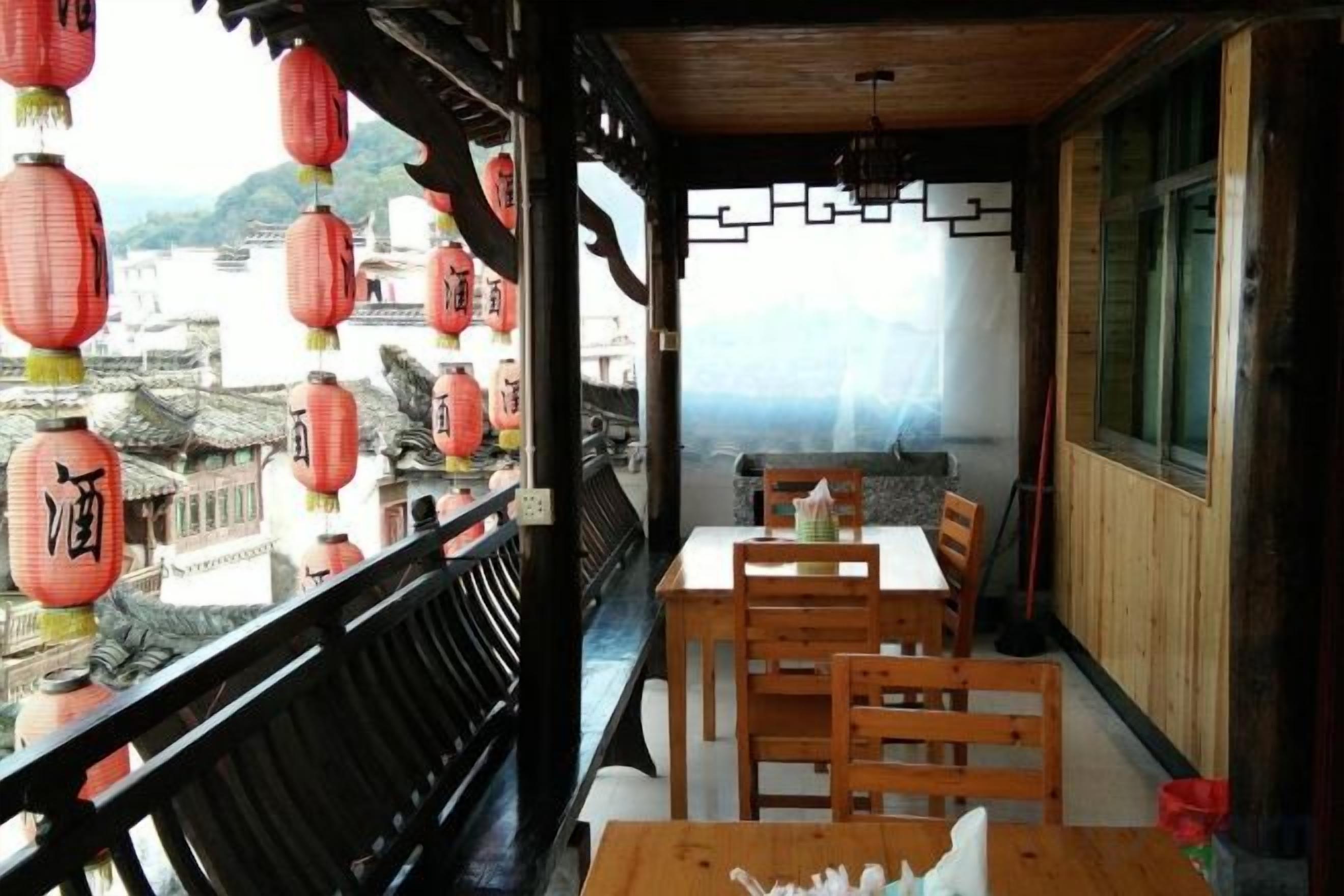 A traditional Japanese-style balcony with wooden furniture and red lanterns, overlooking a historic town.