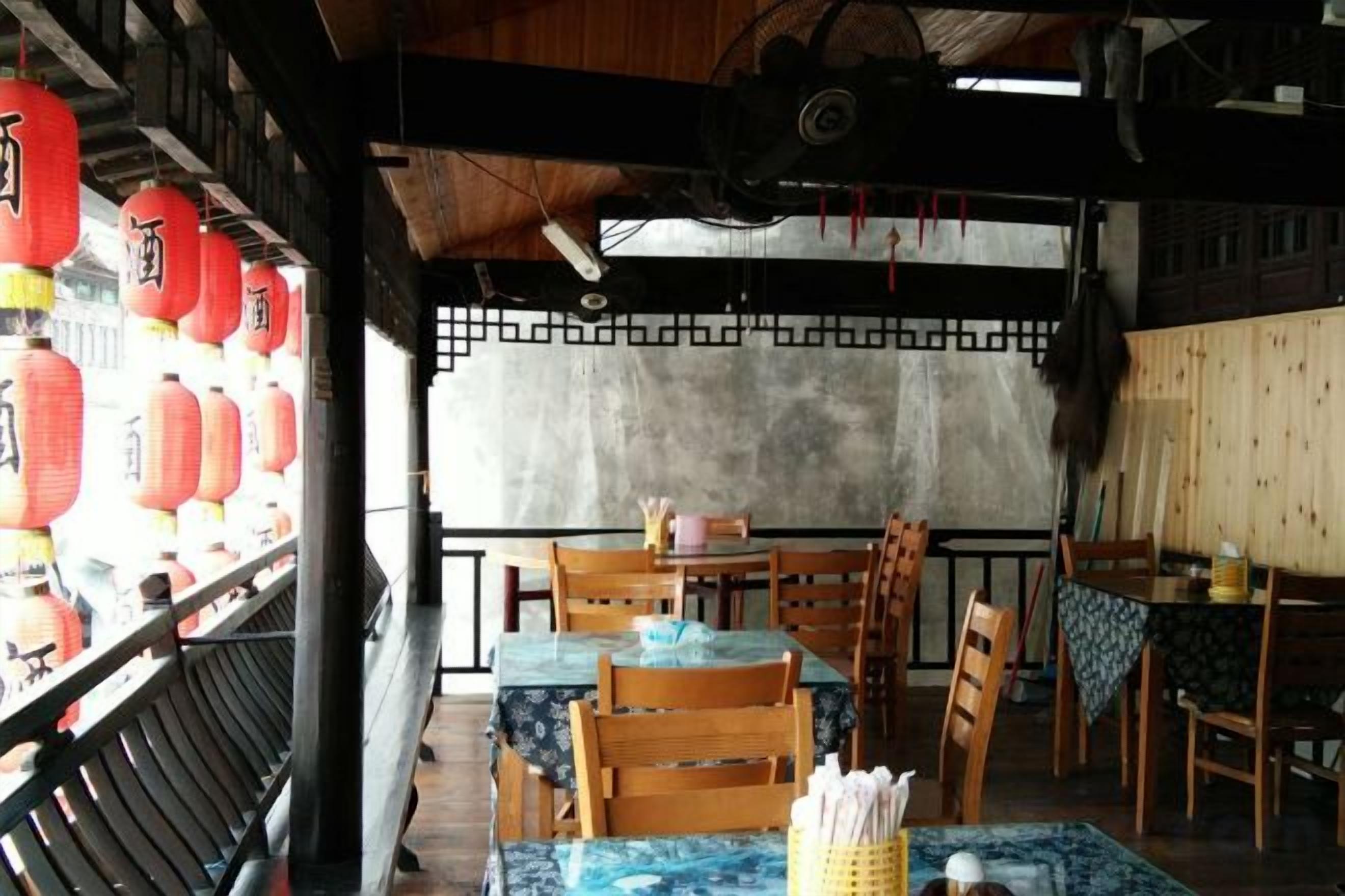 A traditional dining area with wooden tables and chairs, a view of the outside, and red lanterns on the left.