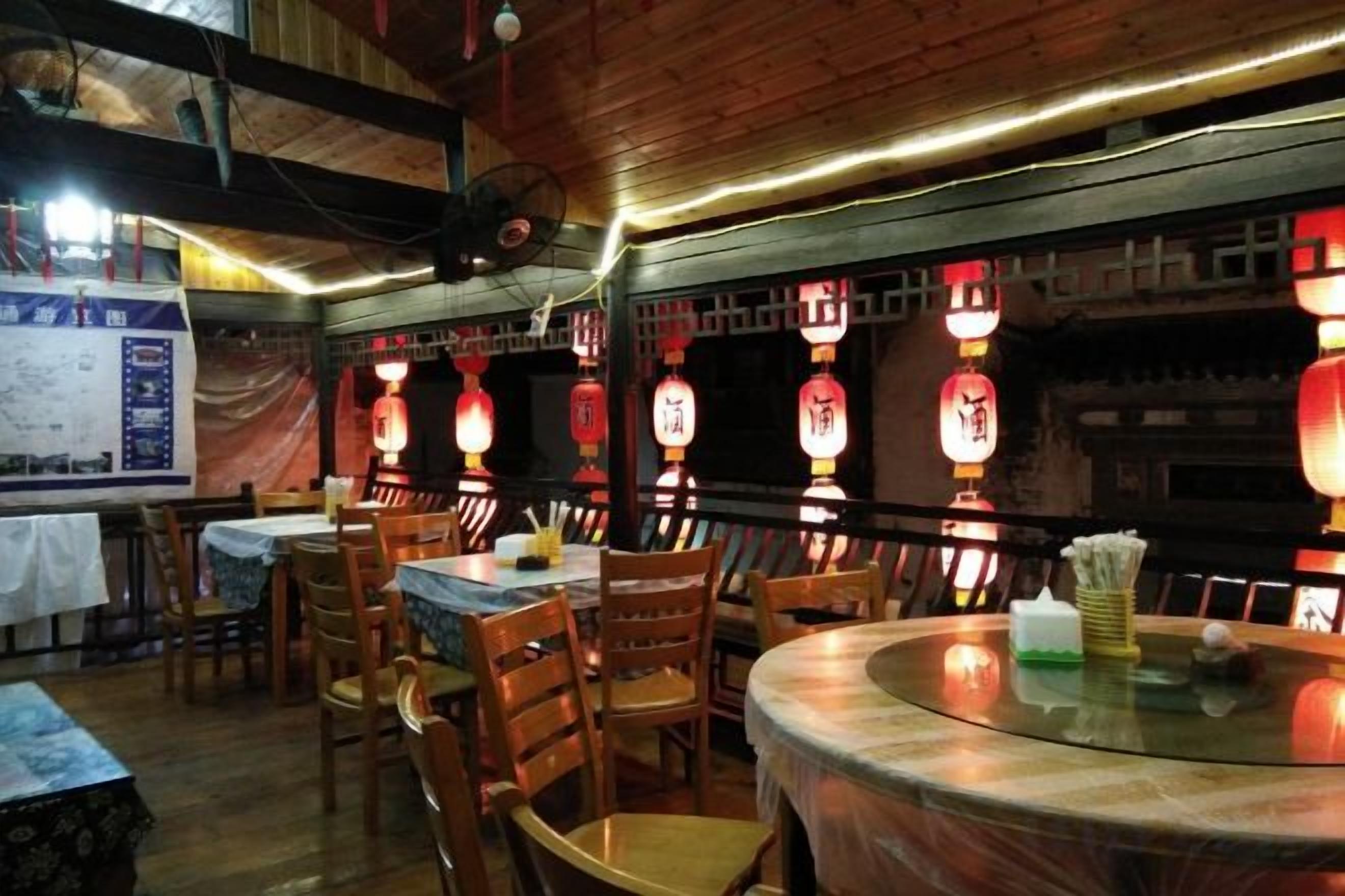 L’intérieur d’un restaurant avec des tables et des chaises en bois, des lanternes traditionnelles et un ventilateur au plafond.