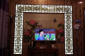 Un téléviseur fixé à un mur en bois, encadré d’un cadre décoratif, un téléphone et un arrangement floral.