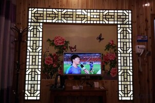 Un televisor montado en una pared de madera con un marco decorativo, un teléfono y un arreglo floral.