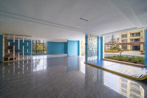 Un hall de hotel amplio y moderno, con una decoración azul y blanca, un ventanal con vistas a la ciudad y un suelo limpio y pulido.