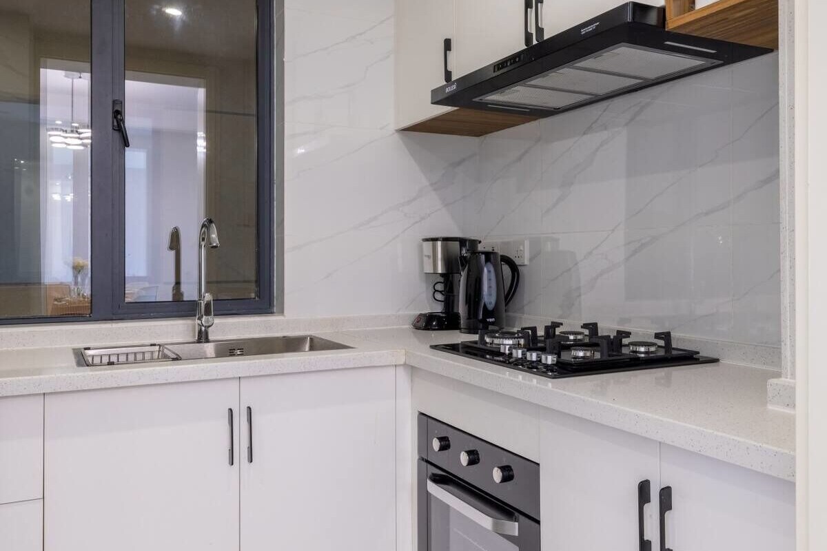 Una cocina moderna con armarios blancos, estufa a gas, cafetera y horno empotrado.