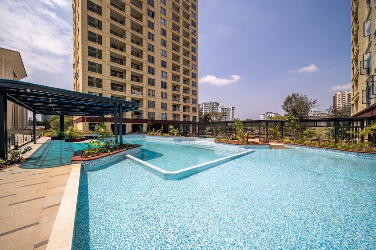 A rooftop swimming pool with a clear blue water feature, surrounded by high-rise buildings and a covered seating area.