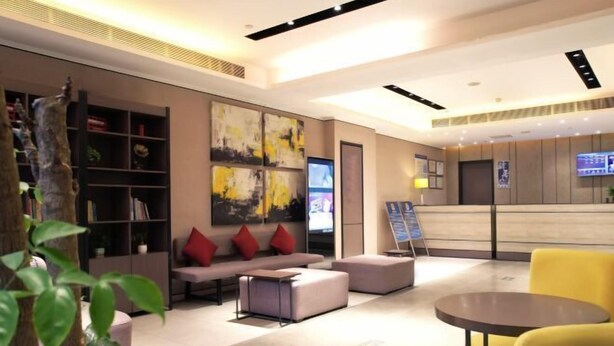 A modern lobby with a sofa, ottoman, and a small table. There is a bookshelf and a TV on the wall. - Ease Hotel (Beijing Liangxiang University Town) (Beijing)