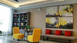 A modern lobby with two yellow armchairs, a grey sofa with red cushions, a bookshelf, and abstract art on the wall. - Ease Hotel (Beijing Liangxiang University Town) (Beijing)