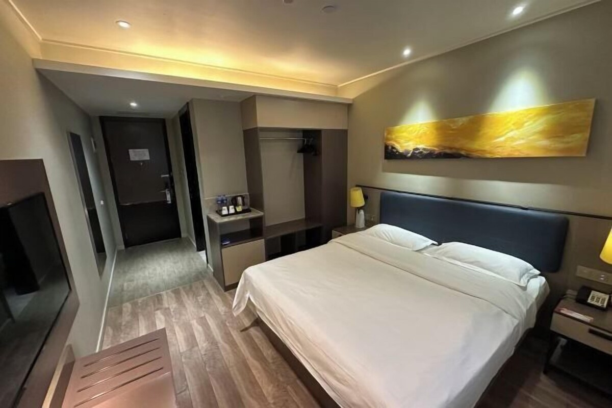 Ein Hotelzimmer mit einem großen Bett, einem Schreibtisch, einem Sessel, einem Fernseher und einem Bild an der Wand.