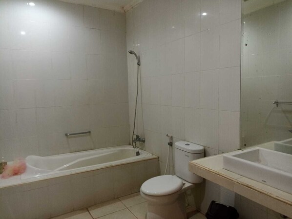 A bathroom with a bathtub, toilet, and sink, all in a neutral color scheme. - Wana Ukir (Sukawati)