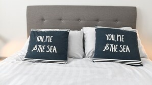 Una cama con dos almohadas que dicen "YOU, ME & THE SEA".