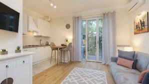 A modern living room with a grey sofa, a flat-screen TV, a dining area with a table and chairs, and a balcony with a sliding door. - Apartment in Baveno with Lake Maggiore Views (Baveno)