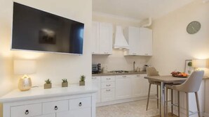 A modern kitchen with white cabinets, a flat-screen TV, a dining area with a table and chairs, and a clock on the wall. - Apartment in Baveno with Lake Maggiore Views (Baveno)