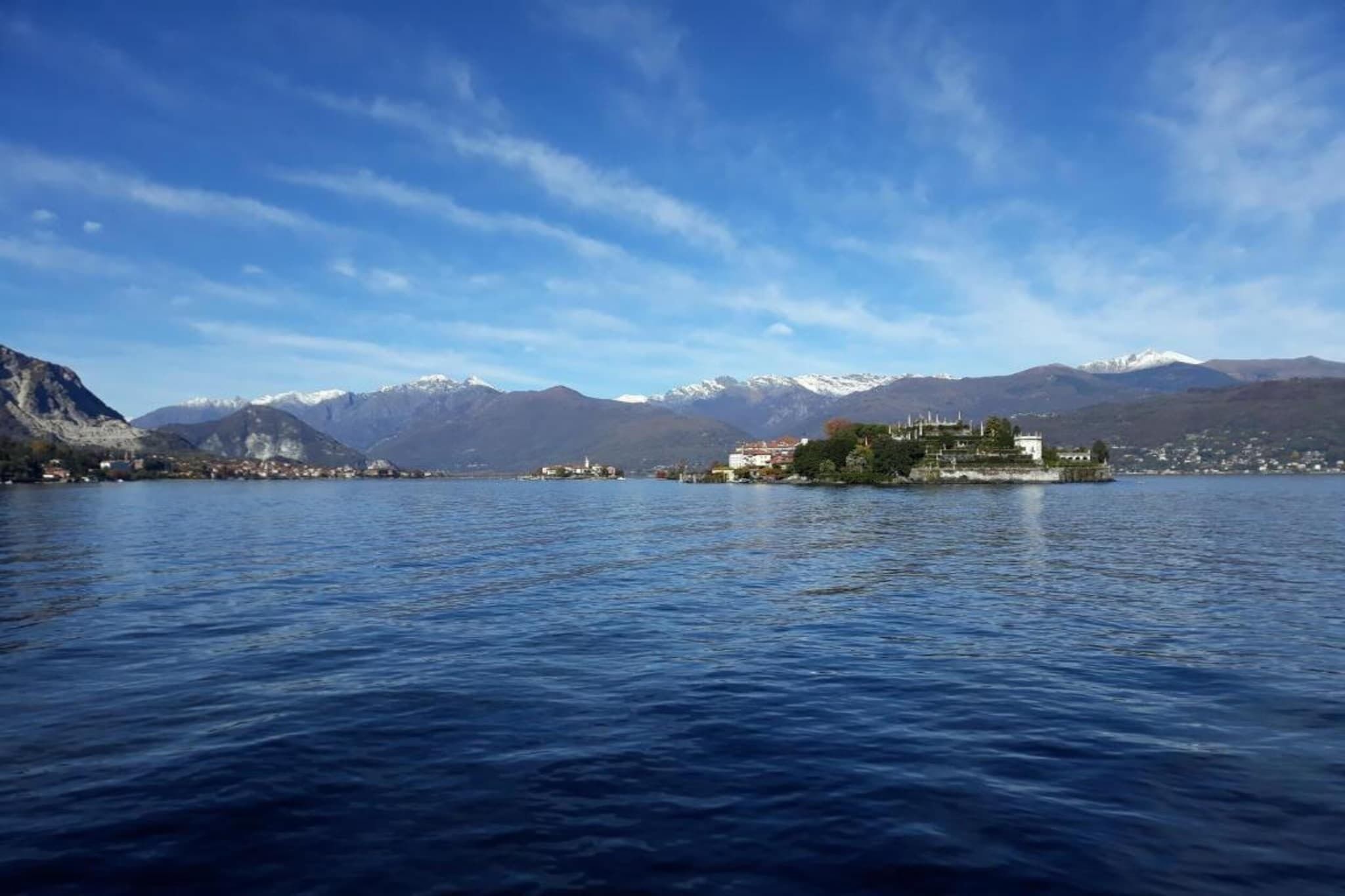 A lake with a small island featuring a white building and a church, surrounded by mountains and clear skies.