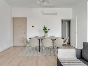 Ein modernes Wohnzimmer mit Esstisch, vier Stühlen, einer Couch, einer Zimmerpflanze und einem Deckenventilator.