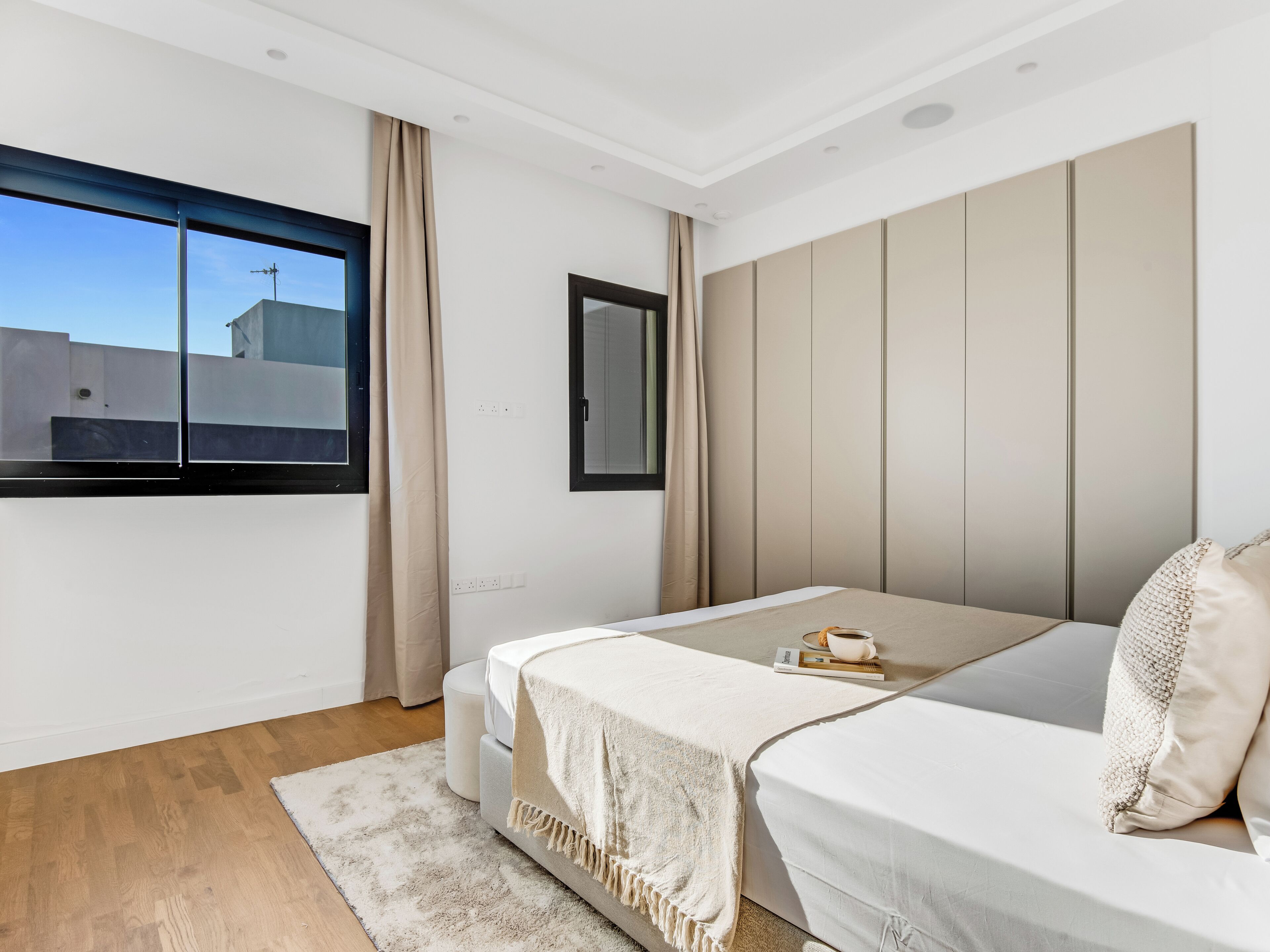 A modern bedroom with a large window, a bed, a bedside table, and a wardrobe.