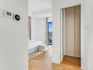 Ein modernes Hotelzimmer mit Bett, einer kleinen Sitzecke und Blick auf die Stadt durch ein großes Fenster.